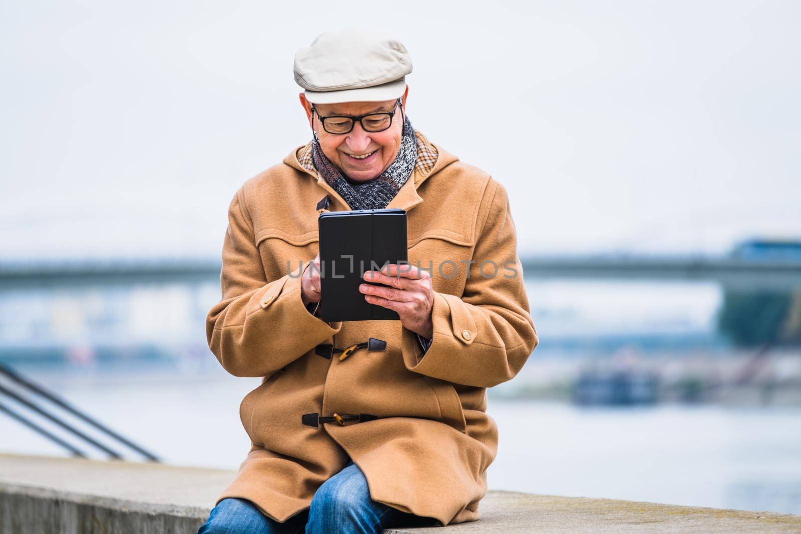 Outdoor portrait of cheerful senior man in winter coat who is using digital tablet.