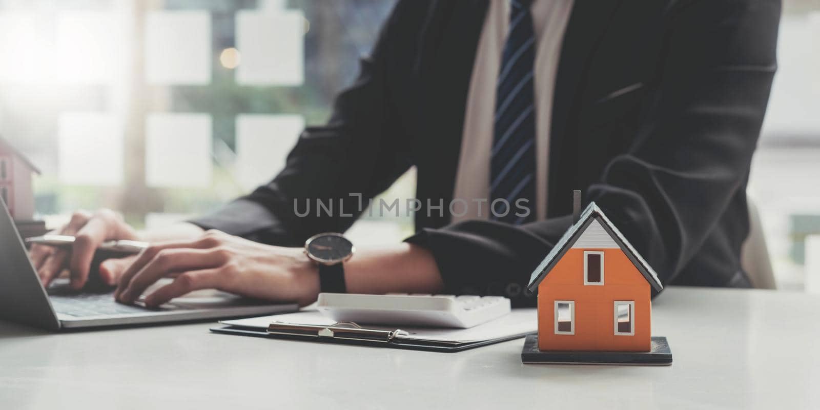 Photo of a house model putting on a clipboard at the wooden working desk over a real estate using a computer laptop as a background. by wichayada