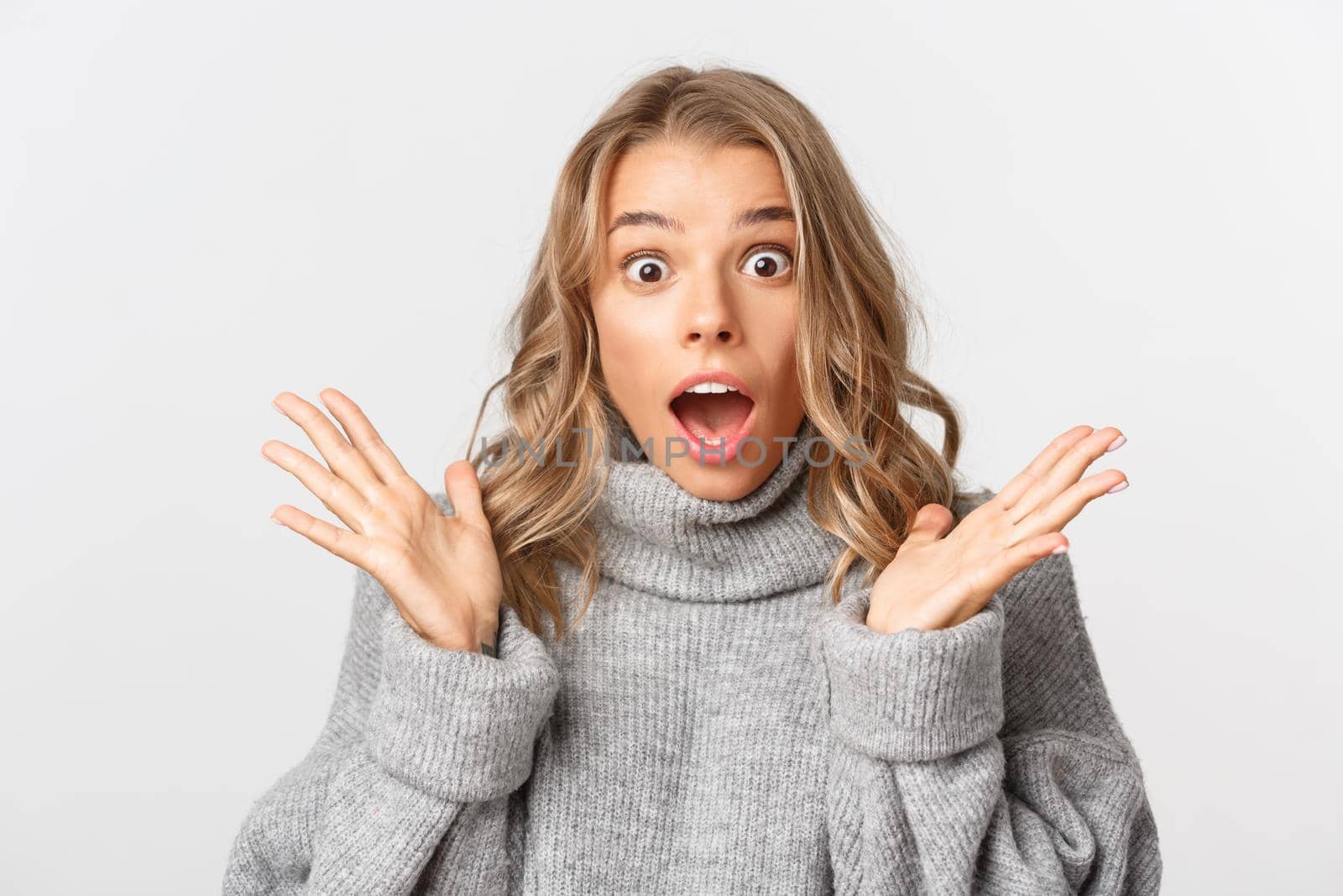 Close-up of shocked gasping girl in grey sweater, open mouth amazed, standing over white background by Benzoix