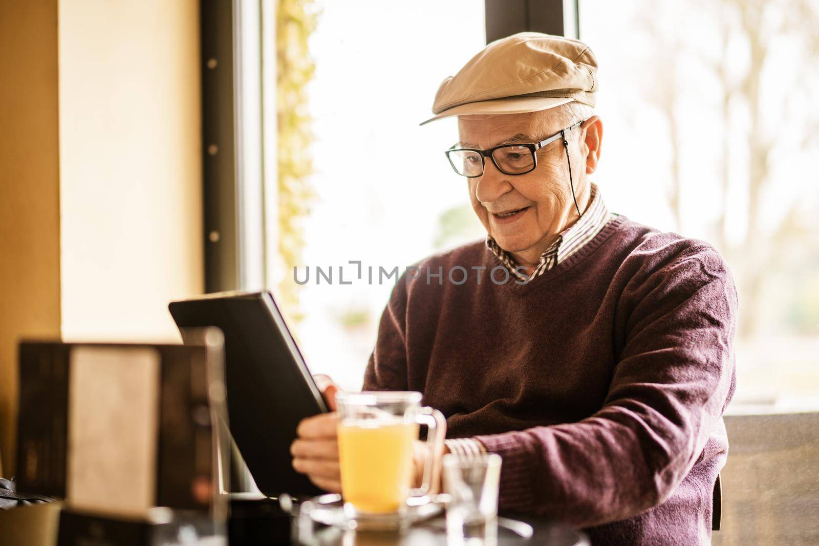 Senior man is sitting in cafe and using digital tablet.