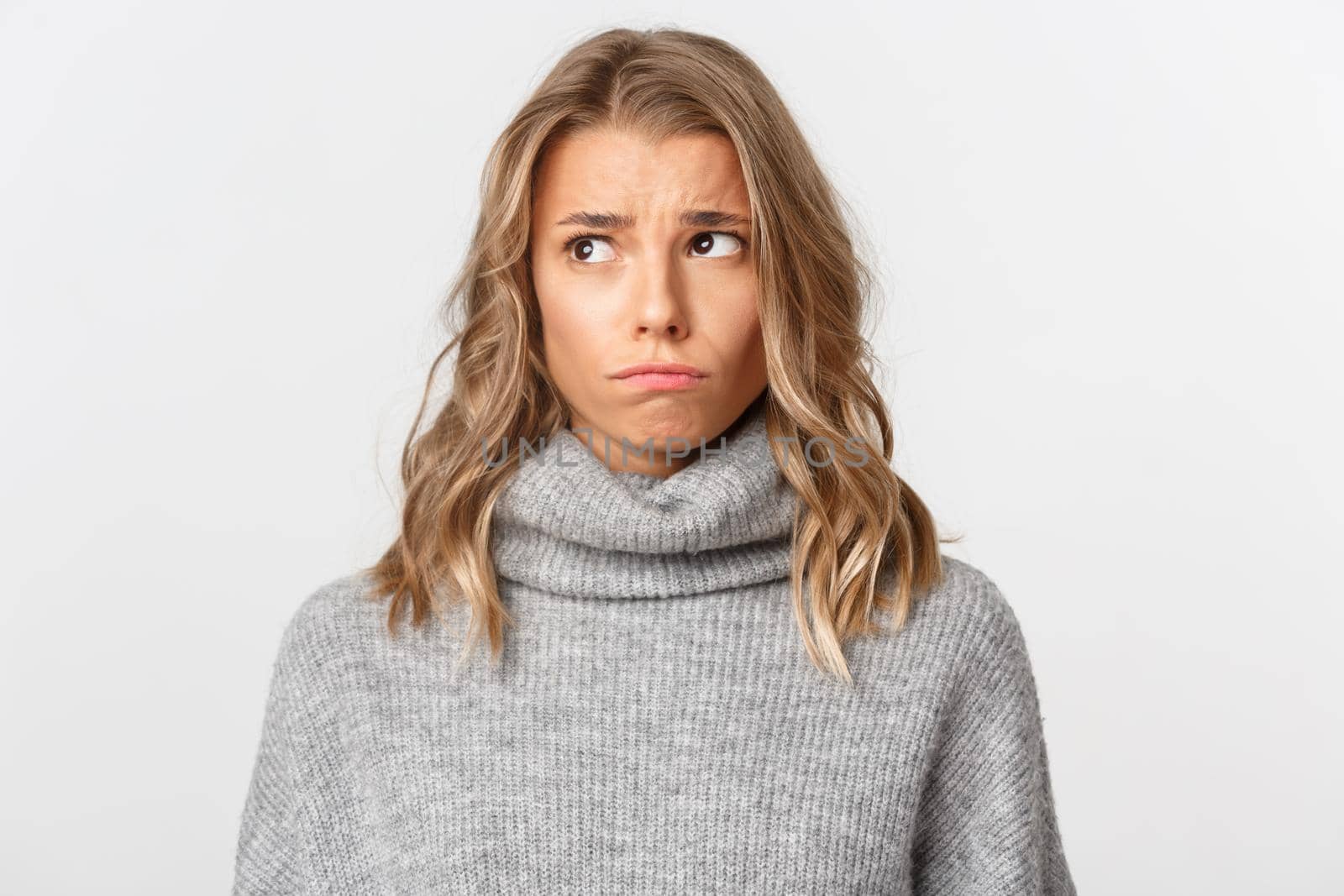 Close-up of attractive gloomy girl with blond short hairstyle, looking sad at upper left corner, standing over white background.