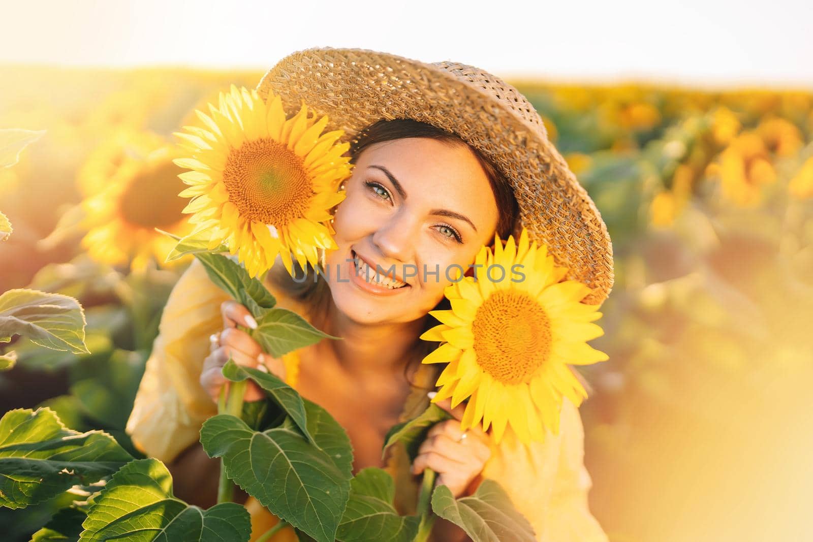 Beautiful young woman in straw hat posing with sunflowers. Blooming field. Happy smiling girl. Trendy outfit, vintage retro style. High quality photo
