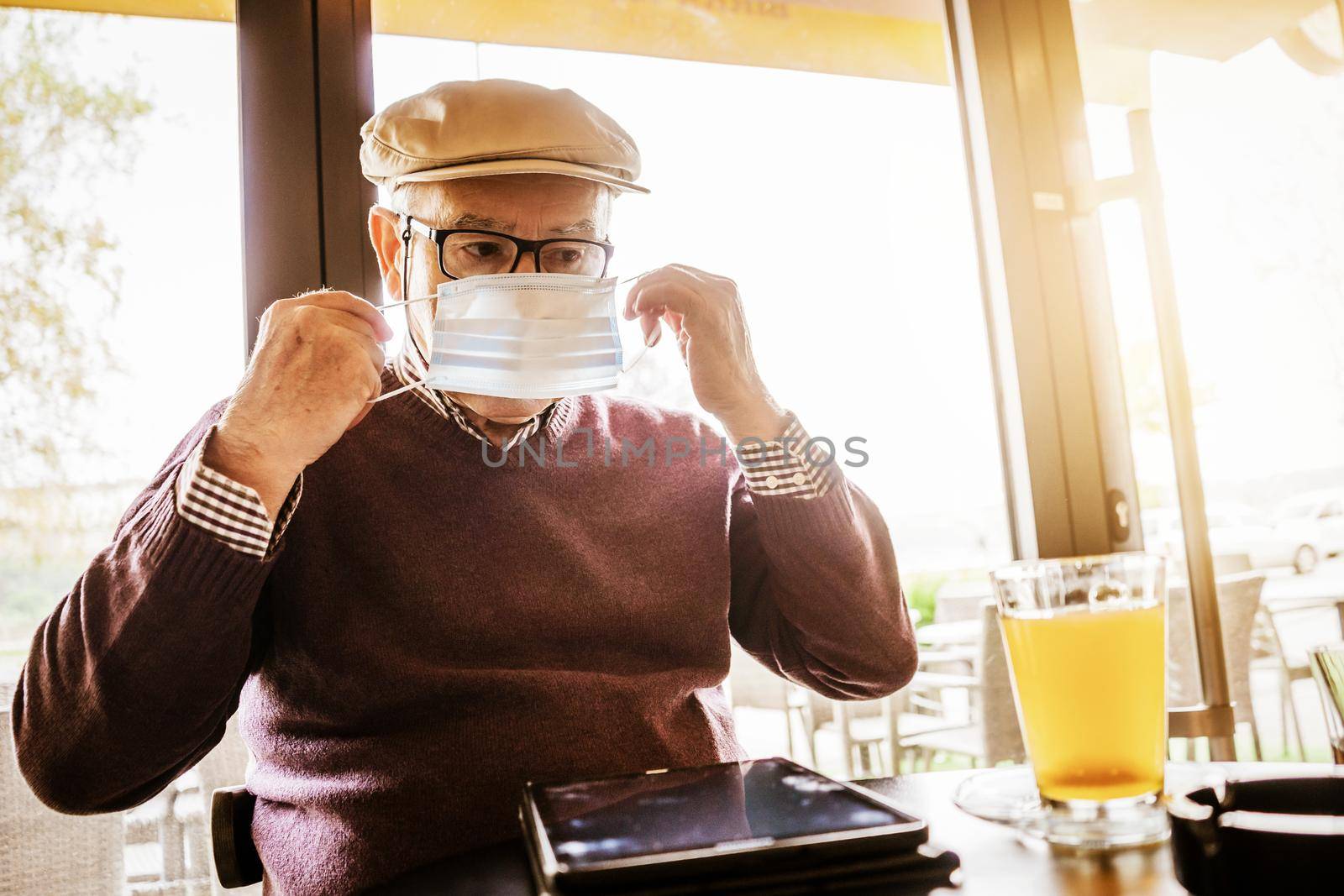 Senior man is sitting in cafe with face protection mask. Covid 19 prevention concept.