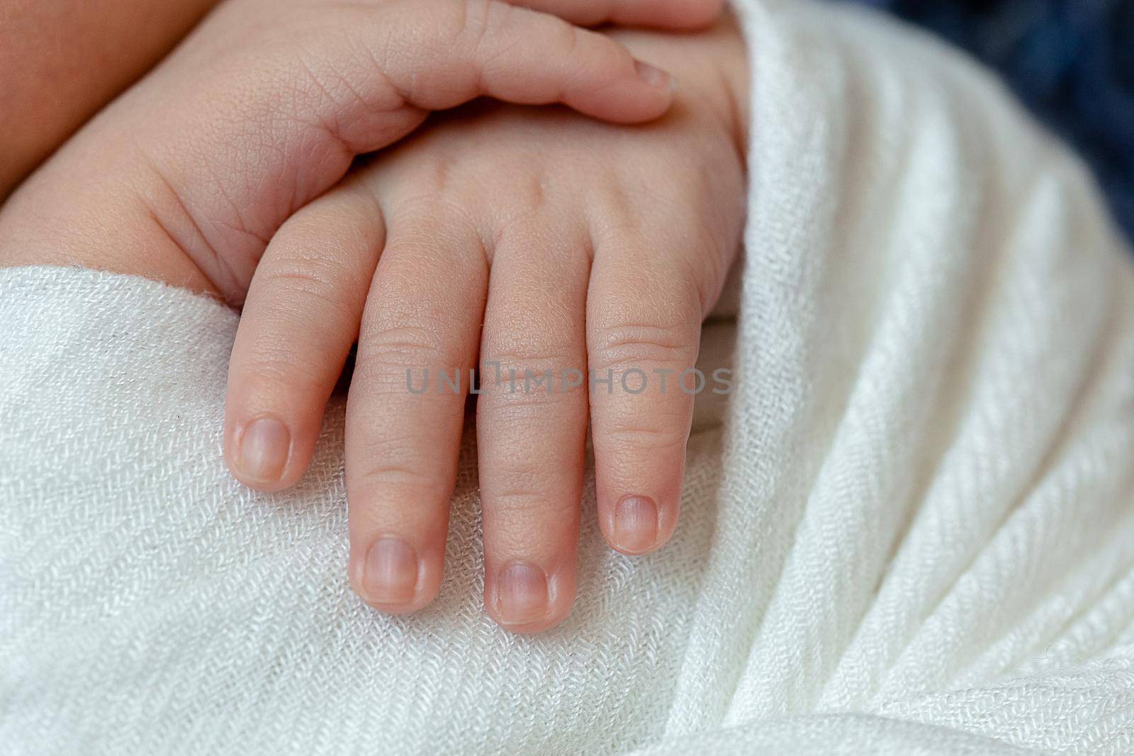 Close-up of little baby handles. The sleeping Newborn boy under a white knitted blanket lies on the blue fur. Newborn. 14 days.