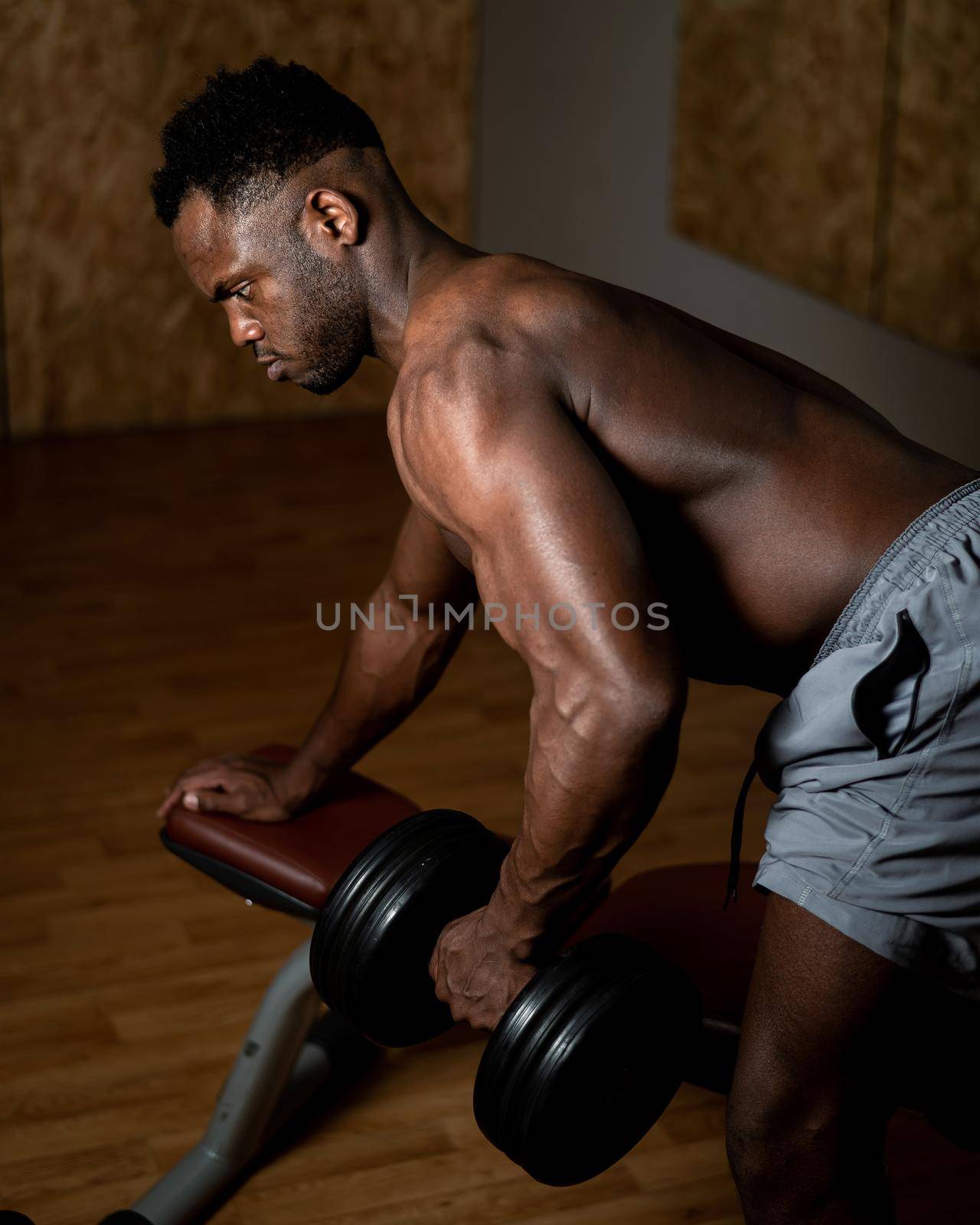 African american man with naked torso doing triceps row with dumbbell on bench. by mrwed54