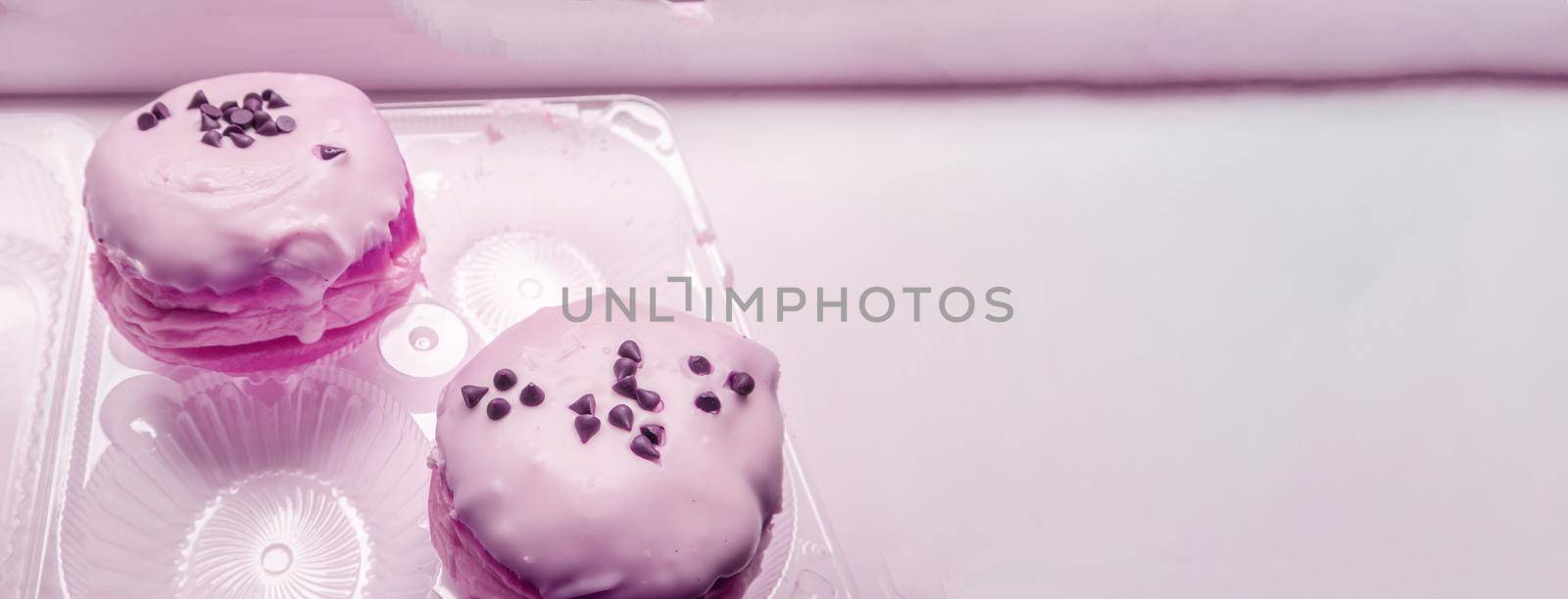 Two delicious donuts with icing sugar and chocolate chips in a transparent plastic container, a banner with a copy of the space on the right, pink tinting by claire_lucia