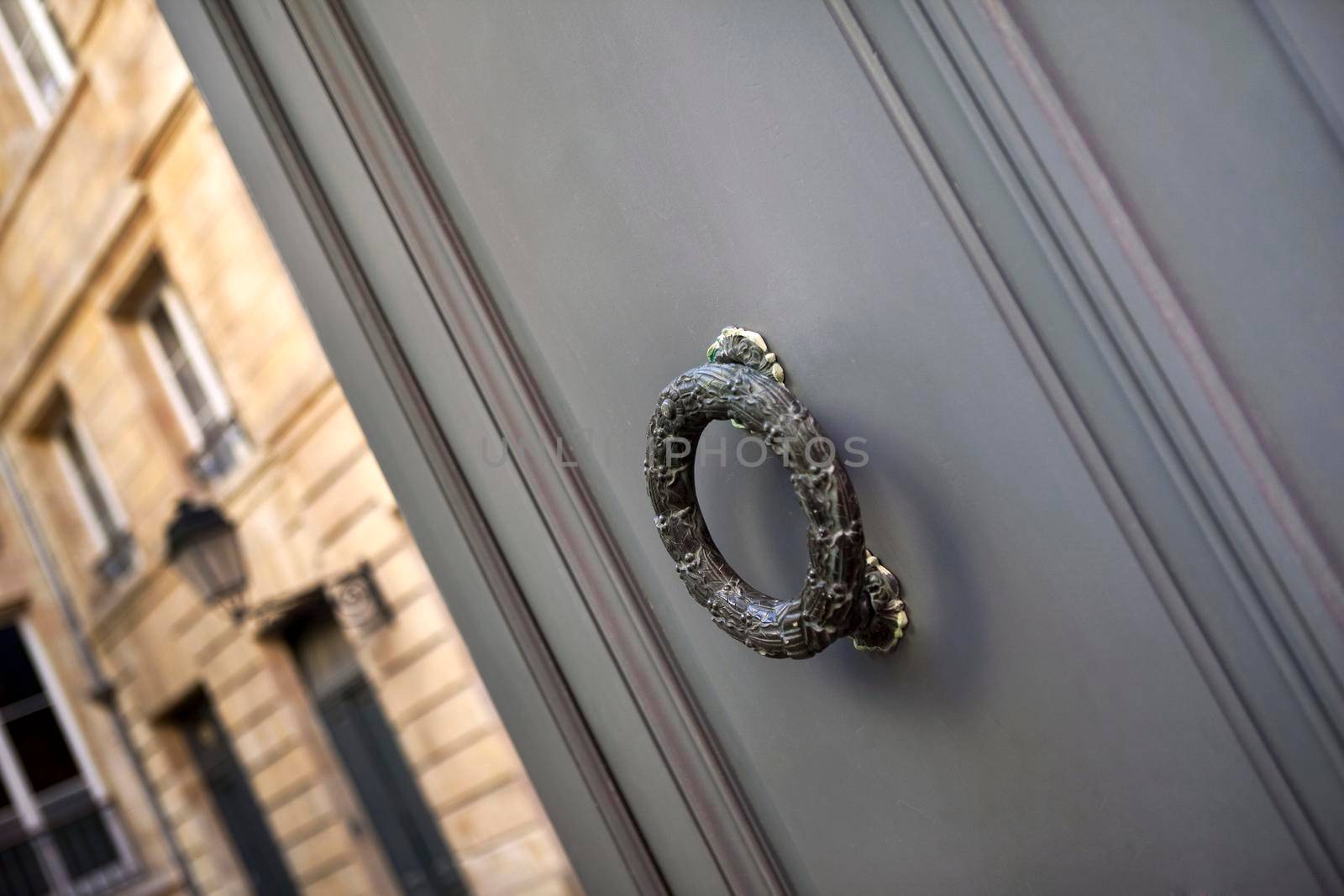 Close up of a bronze door knocker in front of a stoned French mansion