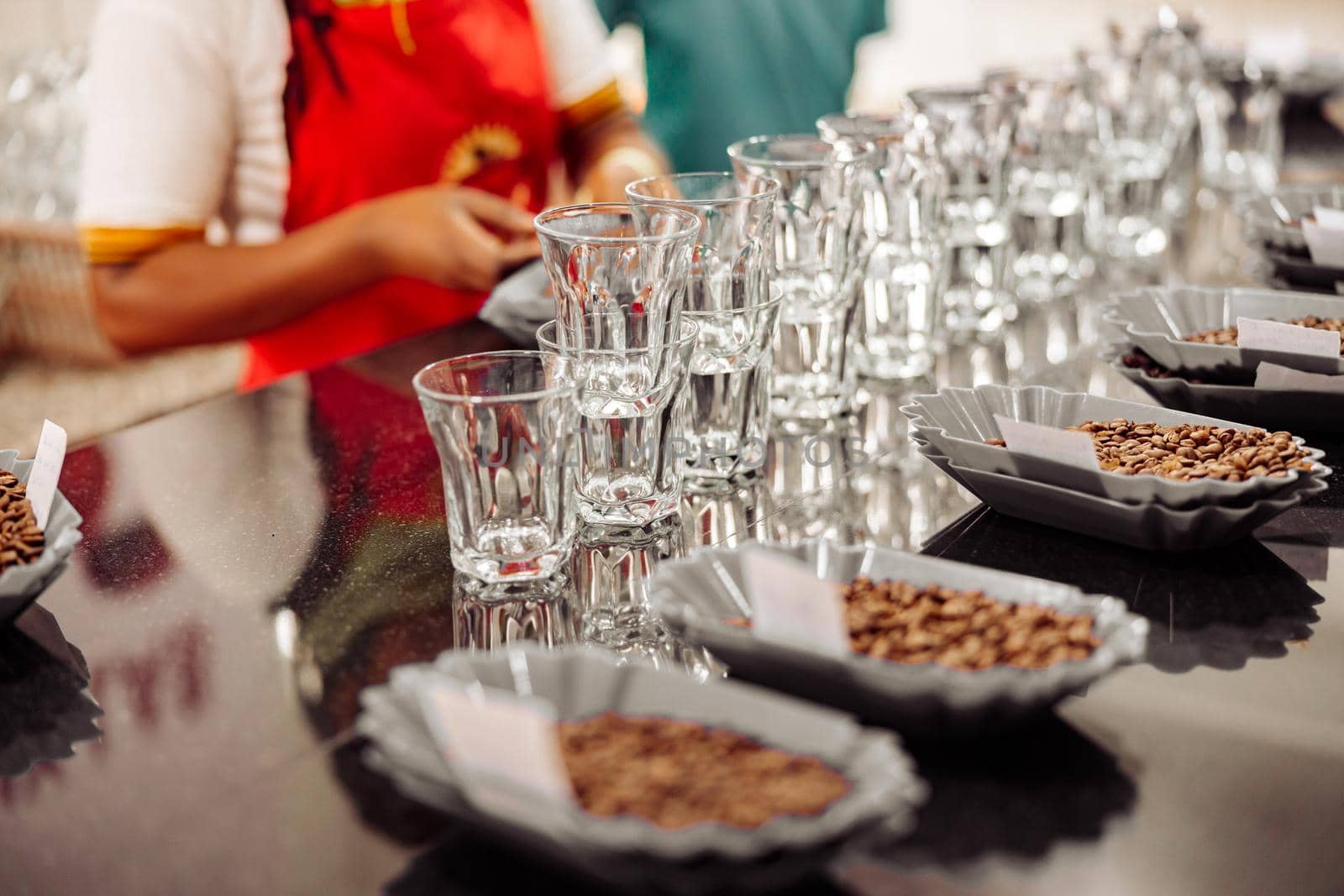 Close up of bowls of coffee beans and empty glasses with female workers on the background