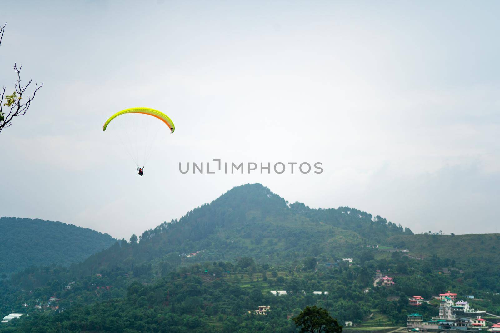 para gliding people with a bright orange yellow glider in the middle of hills mountains near nanital bir billing showing a popular adventure sport for tourists by Shalinimathur