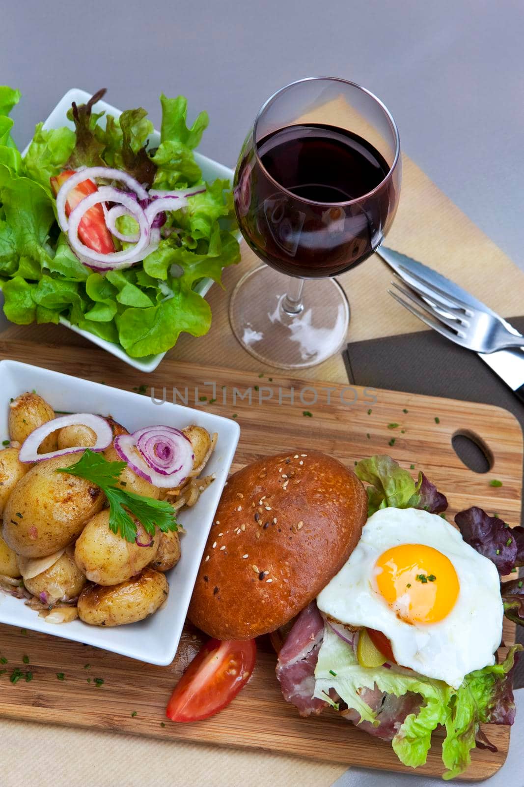 Hamburger, potatoes, egg and green salad on a wooden board