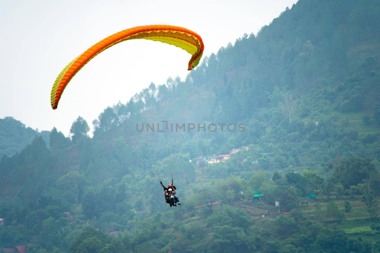 para gliding people with a bright orange yellow glider in the middle of hills mountains near nanital bir billing showing a popular adventure sport for tourists hill station