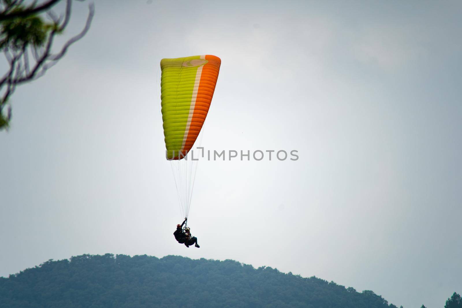 para gliding people with a bright orange yellow glider in the middle of hills mountains near nanital bir billing showing a popular adventure sport for tourists hill station