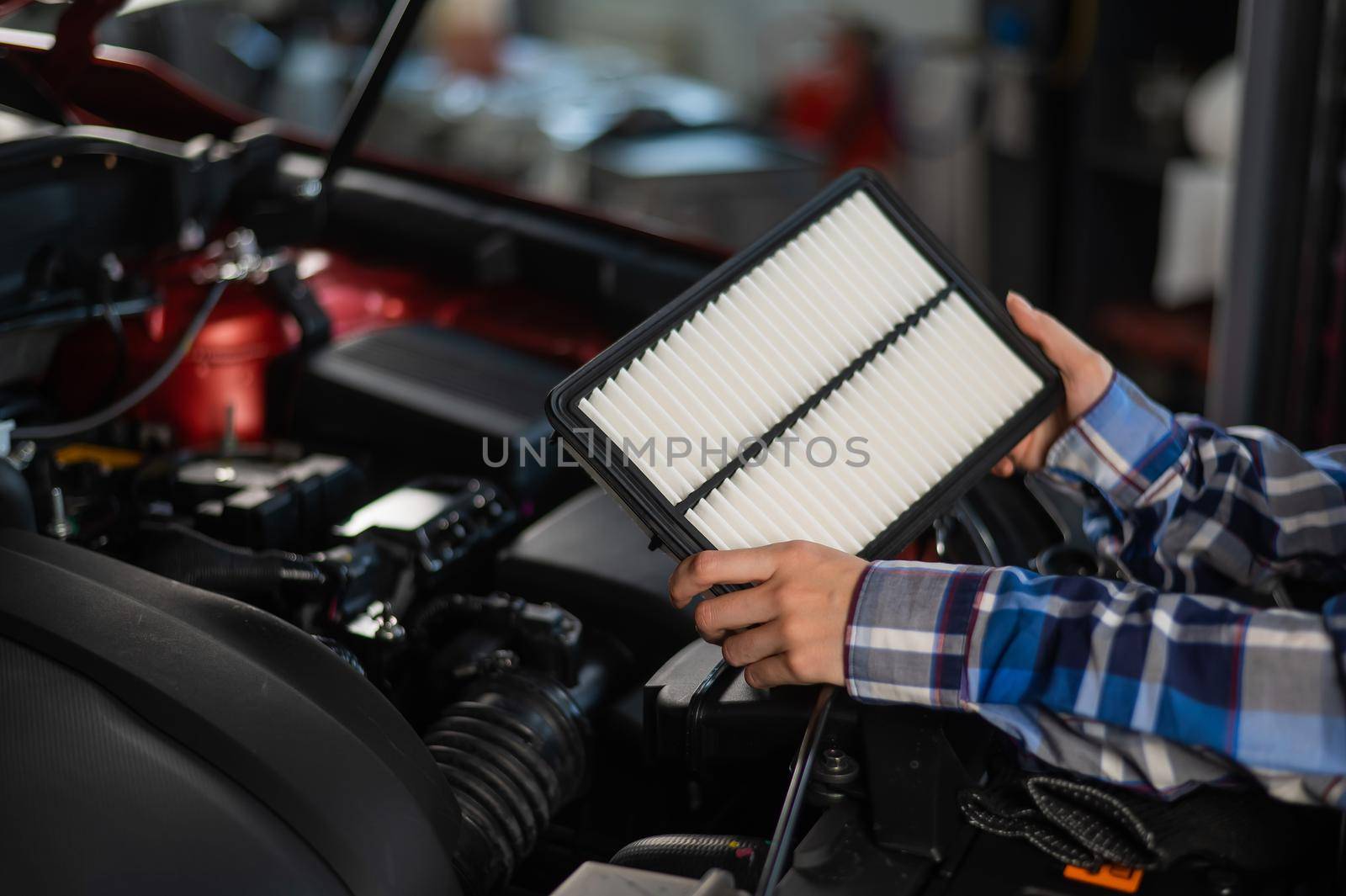 Caucasian female auto mechanic changes the engine air filter in the car