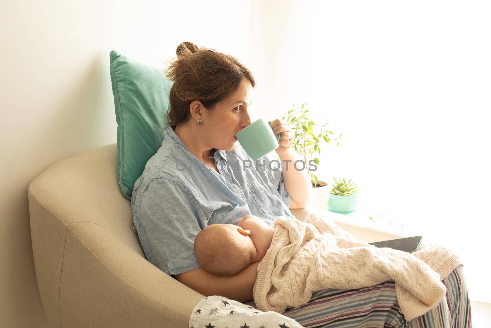 Woman drink tea or coffee during process of breastfeeding of newborn baby by oksix