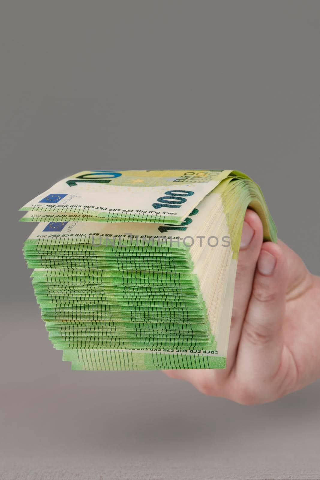 Large stack of euros in hand. Banknotes of 100 euros in a male hand on a uniform background. A man holds out his hand with a stack of banknotes as a concept of a loan, insurance payment or mortgage. by SERSOL