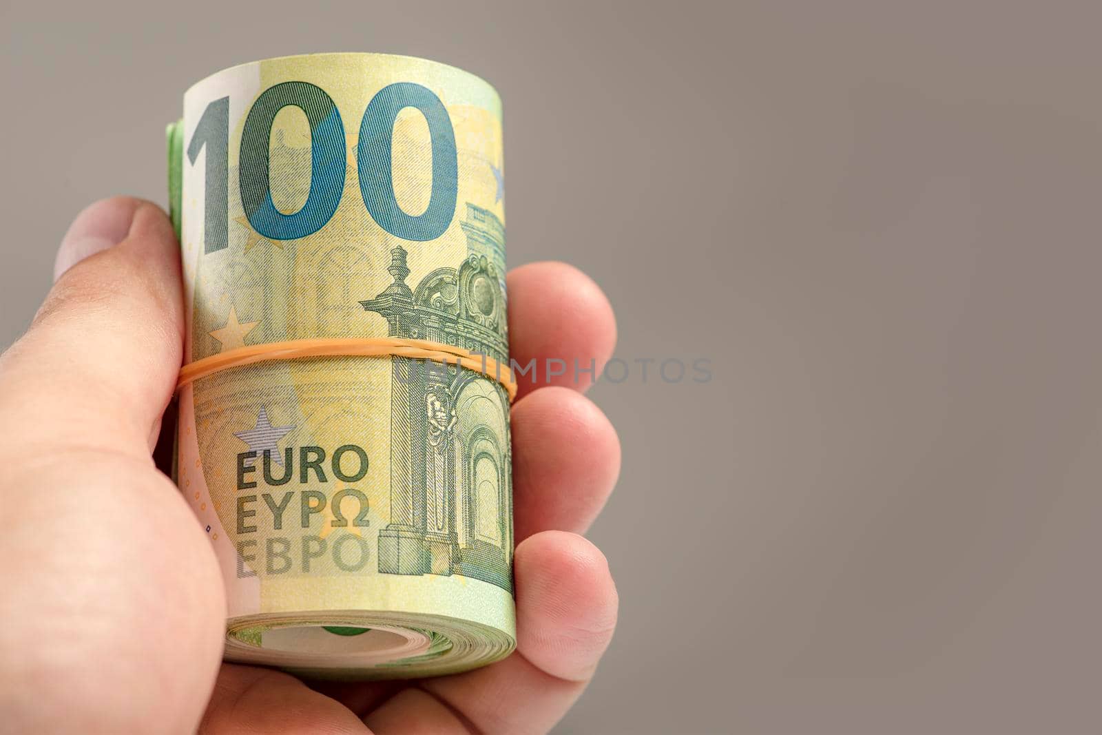 The hand holds a roll of 100 euro banknotes. Euro banknotes rolled up in a white man's hand on a gray background. The concept of financial assistance, real estate purchase, loan or insurance payment
