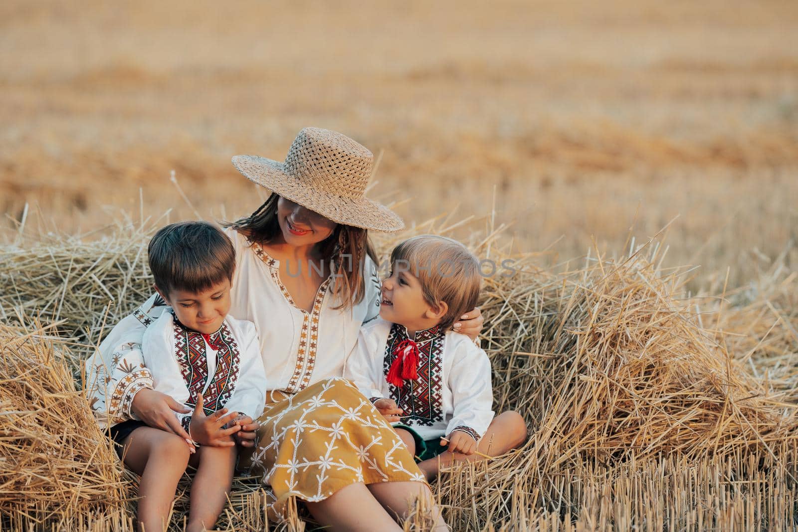 Ukrainian boys and mother sitting together on wheat in field after harvesting. Family, friends holding hands. Children is our future. Happy childhood. High quality photo