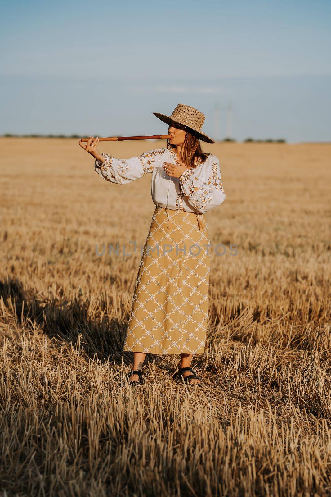 Woman playing on woodwind wooden flute - ukrainian telenka or tylynka in wheat field. Folk music concept. Musical instrument. Musician in traditional embroidered shirt - Vyshyvanka. High quality photo