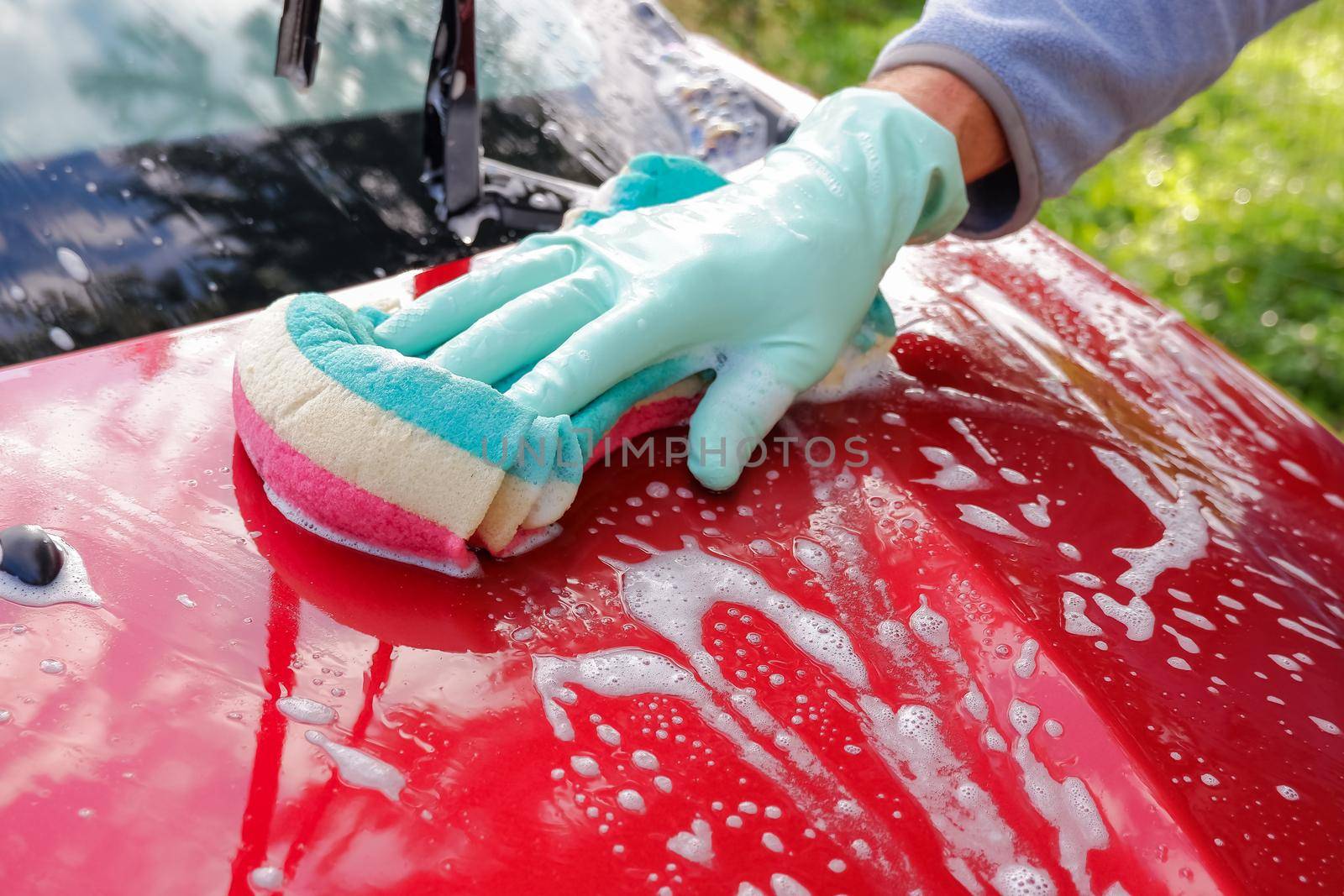 Worker washing red car with sponge on a car wash