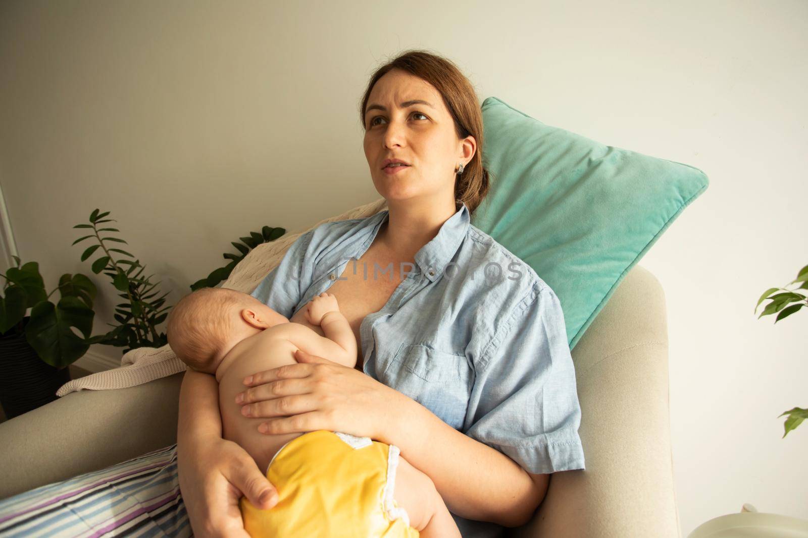 Closeup view newborn baby breastfeeding. Young mother learning how to hold baby, lactation consultant supports mother, helping to adjust baby for comfortable and effectife feeding.