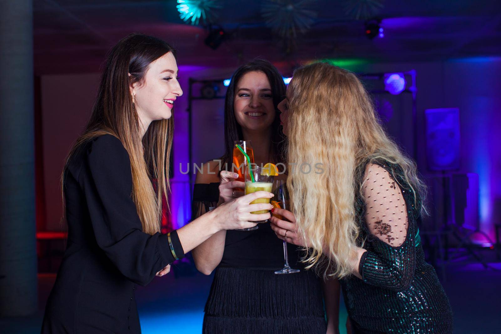 Women have fun and drinking cocktails with fruits in night club. Dance party