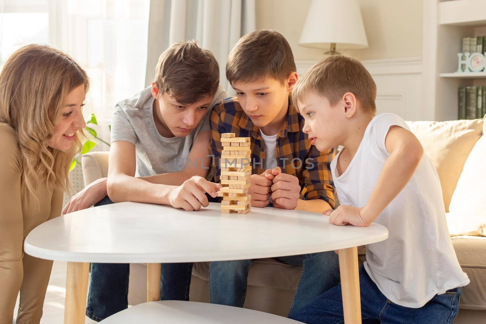 A smiling woman and three boys are enthusiastically playing a board game made of wooden rectangular blocks by Zakharova