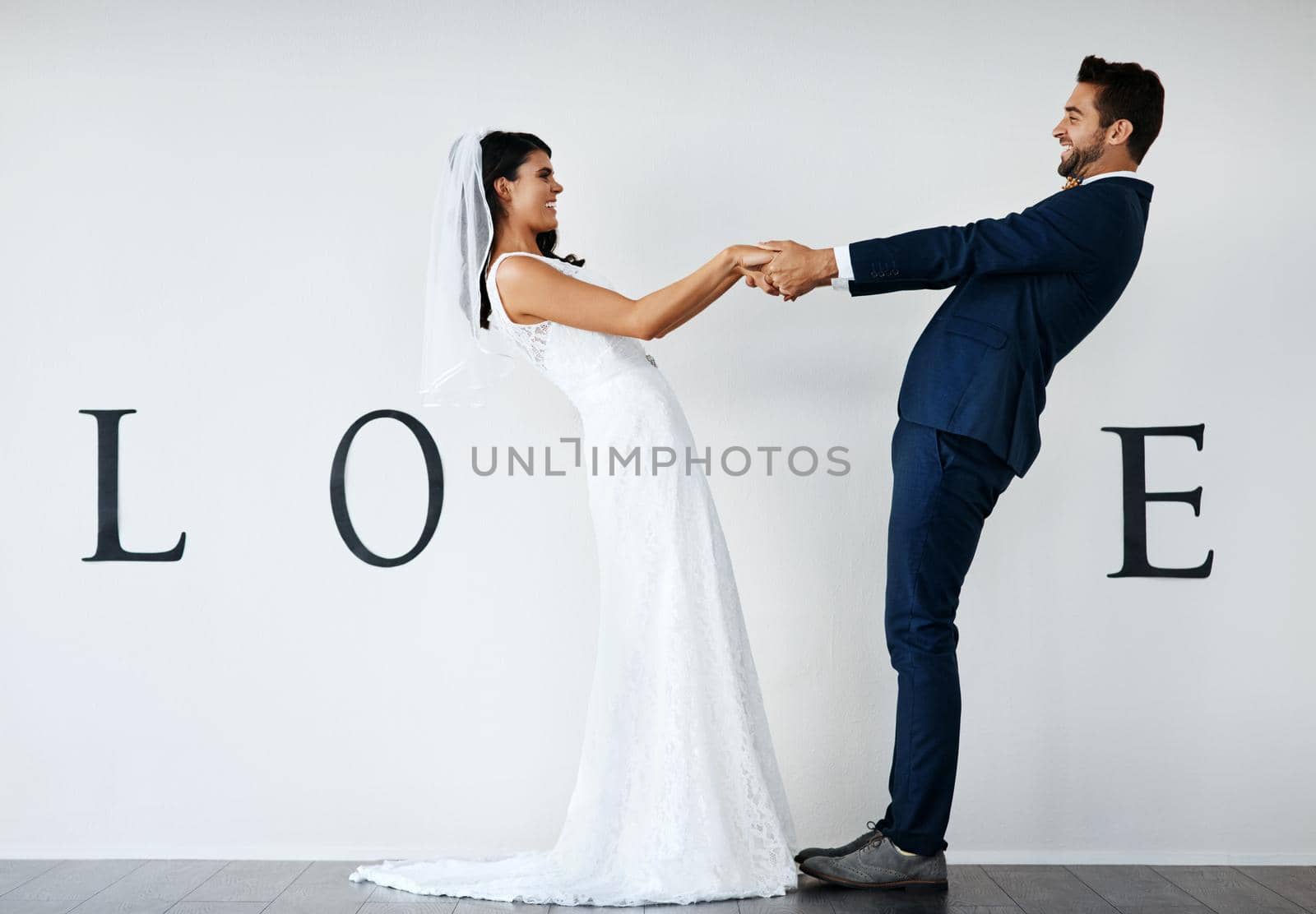 Love spins you around. Concept studio shot of a bride and groom making an V in the word love against a wall