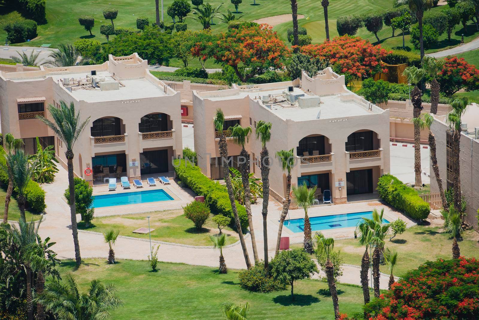 Aerial view over holiday villas with swimming pool in luxury tropical hotel resort with gardens and golf course