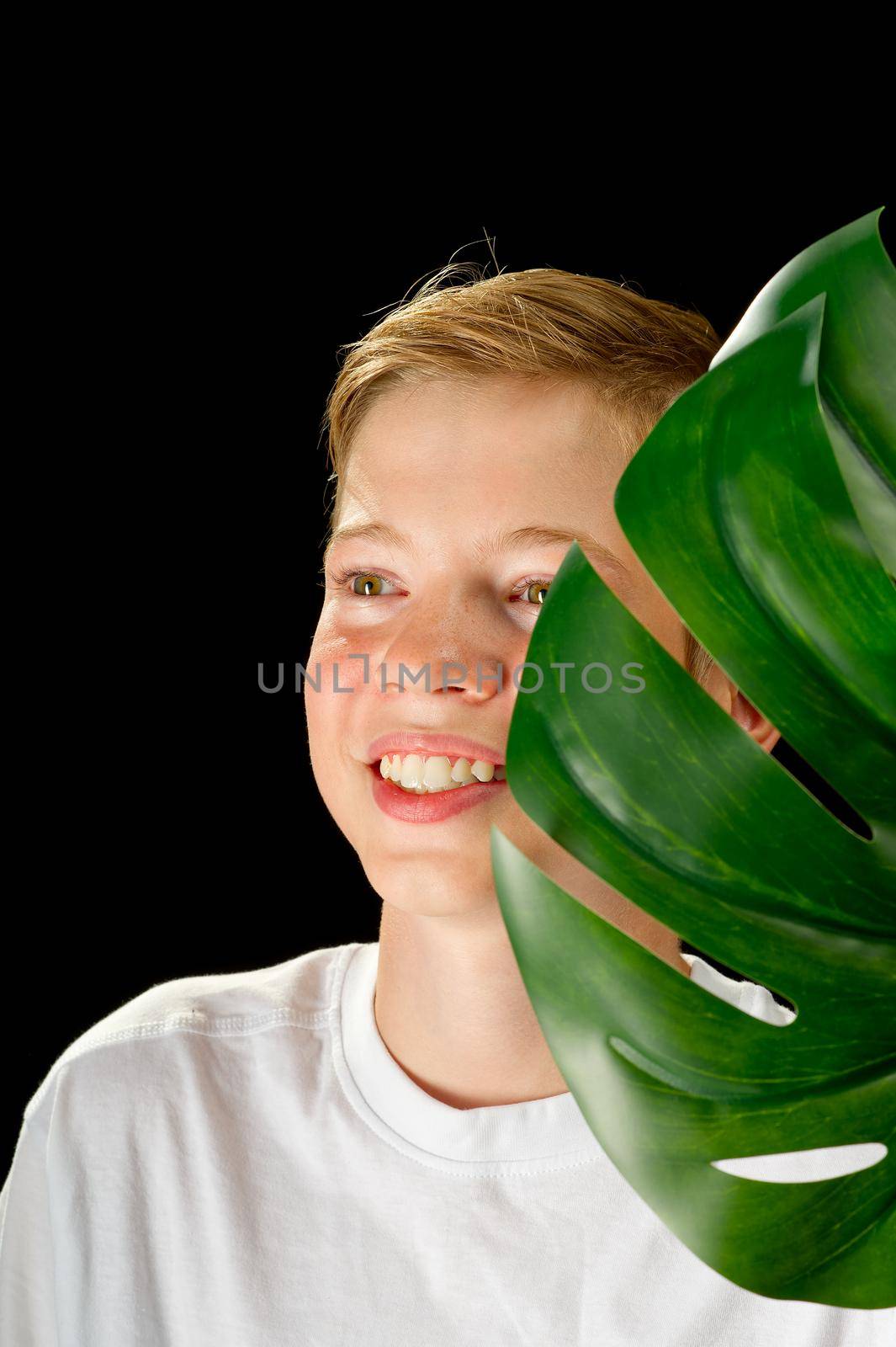Fashion studio portrait of a boy holds green monstera leaf. cosmetology concept for young teenagers. isolated on black background