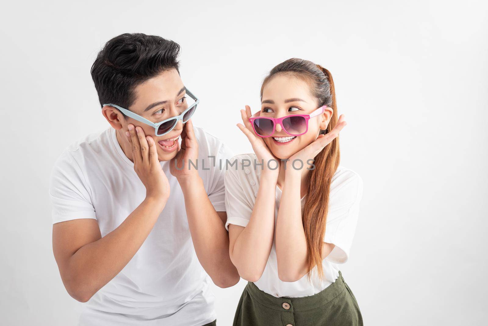 Gesture and people concept - Portrait of happy couple in sunglasses and white t-shirts, touches cheeks with both hands over white background by makidotvn