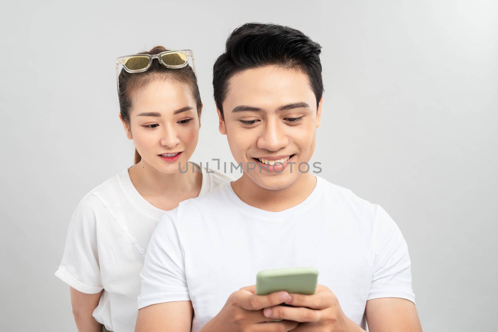 Photo of couple with her looking into her guy screen and him cheating to his lover smiling toothily isolated over white background by makidotvn