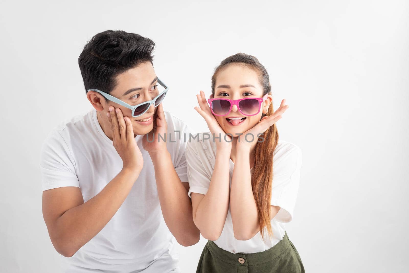 Funny couple  touches cheeks with both hands in casual style clothes and color glasses over white background by makidotvn