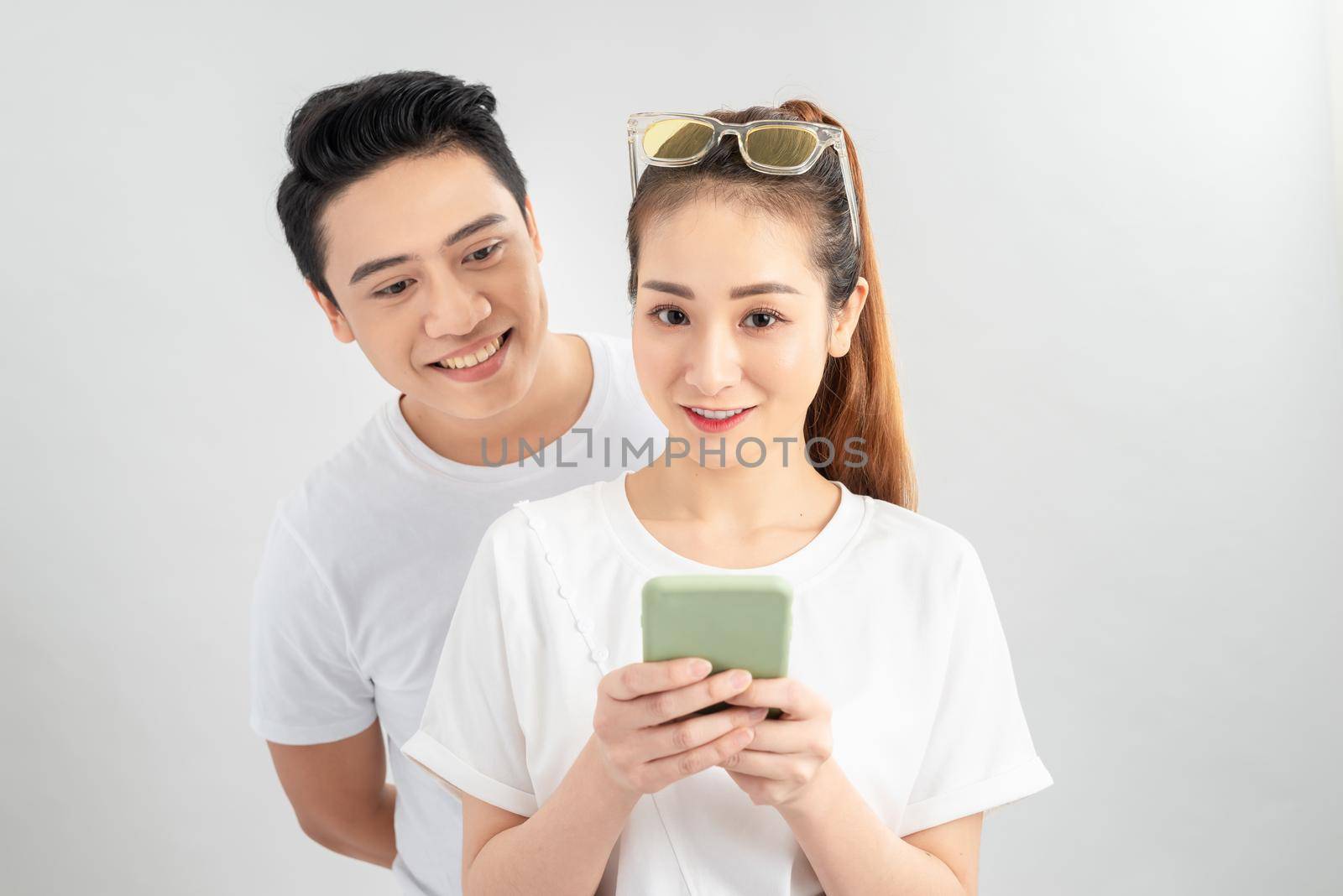Asian couple using smartphone / mobile handset, standing isolated over white background