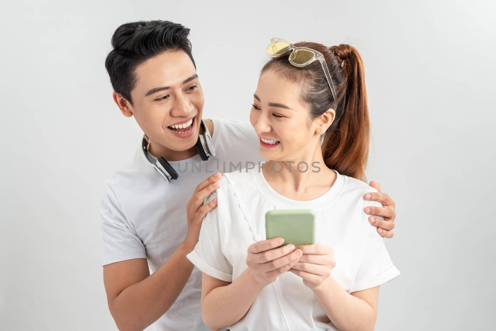 Image of cheerful man smiling while looking at cellphone of his girlfriend isolated overwhite background by makidotvn