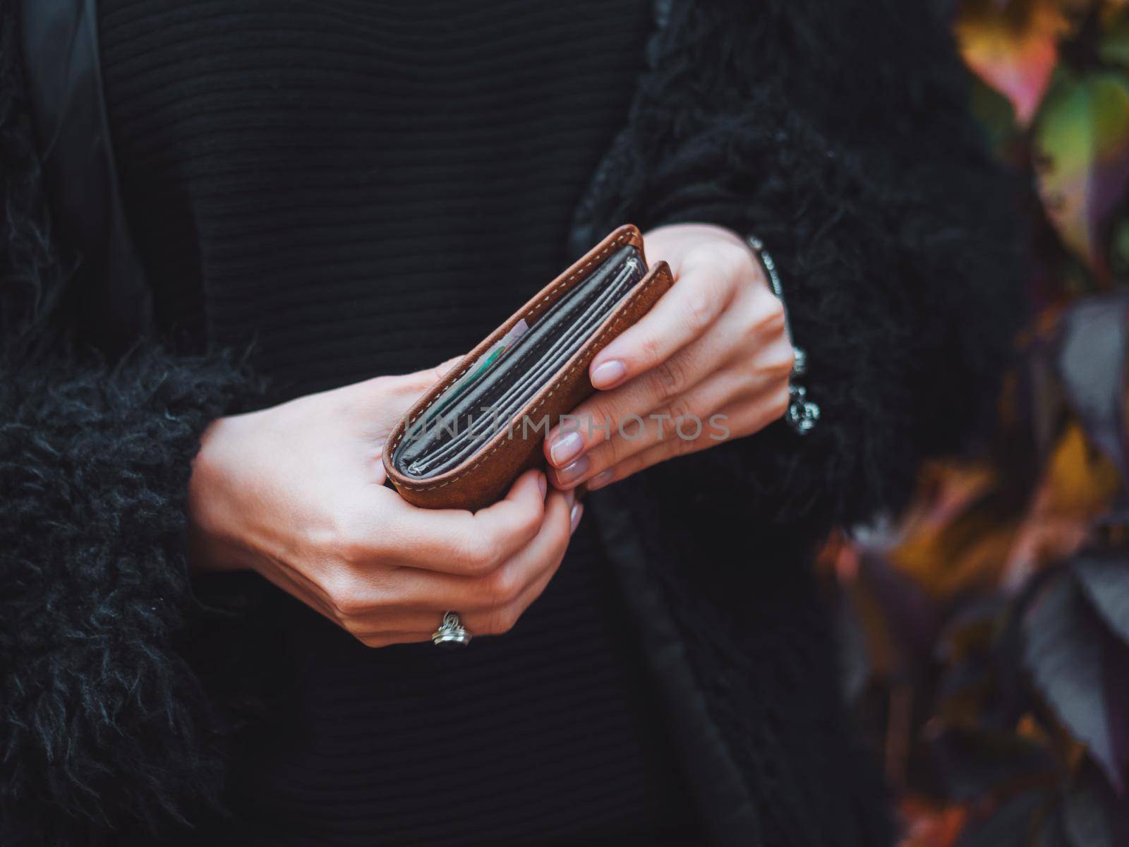 people, saving and finance concept - hands with cash money and wallet in autumn park. Close up hands of young woman with brown purse.