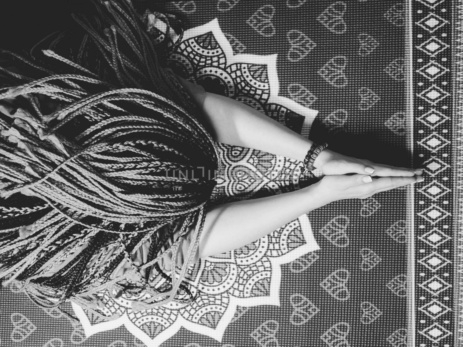 Concentrated woman with blue african braids praying with wooden rosary mala beads. Namaste. Close up hands on yoga mat with mandala. Top view.