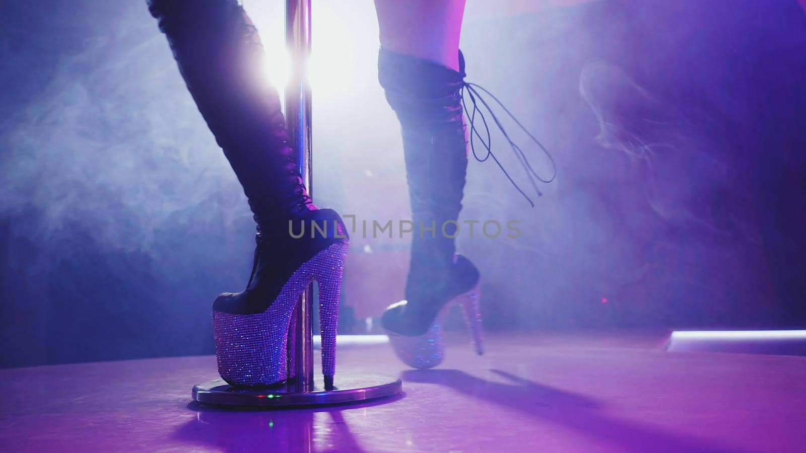 Sexy woman in high boots on platform and heel with rhinestones. Fringe skirt with pendants made of shiny stones. striptease dancer moving on stage in strip night club,