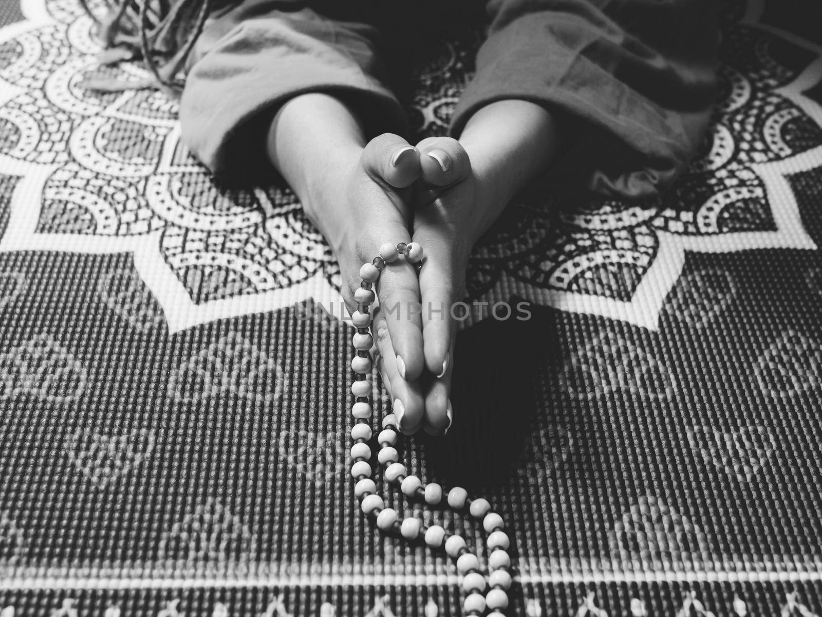 Concentrated woman praying with wooden rosary beads on yoga mat with mandala. Namaste. Close up hands. gratitude concept.