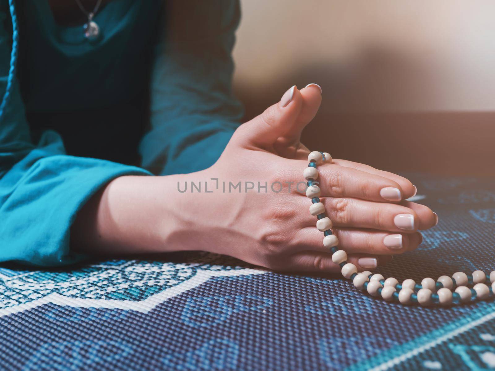 Concentrated woman praying with wooden rosary beads on yoga mat with mandala. Namaste. Close up hands. gratitude concept.