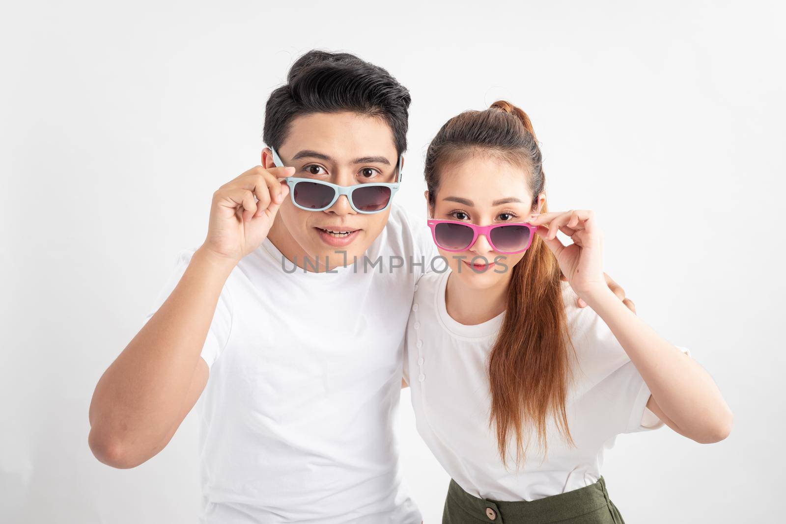 Beautiful cute adorable surprised couple putting colorful spectacles down showing wow emotion over yellow background, isolated