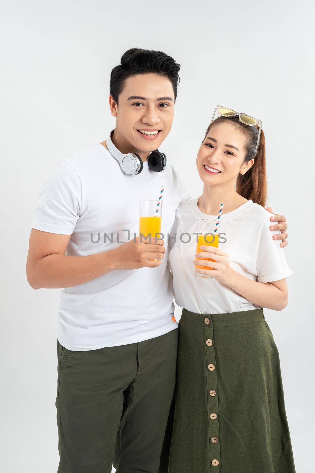 Stylish couple in casual clothes is drinking juice, looking at camera and smiling on white background by makidotvn