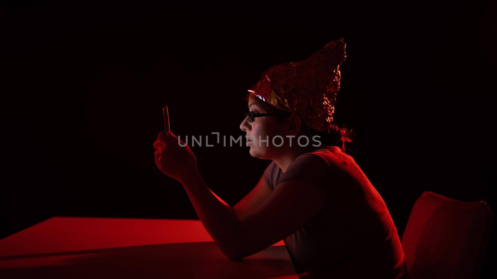 Paranoid caucasian woman using smartphone wearing tinfoil hat. Conspiracy theory