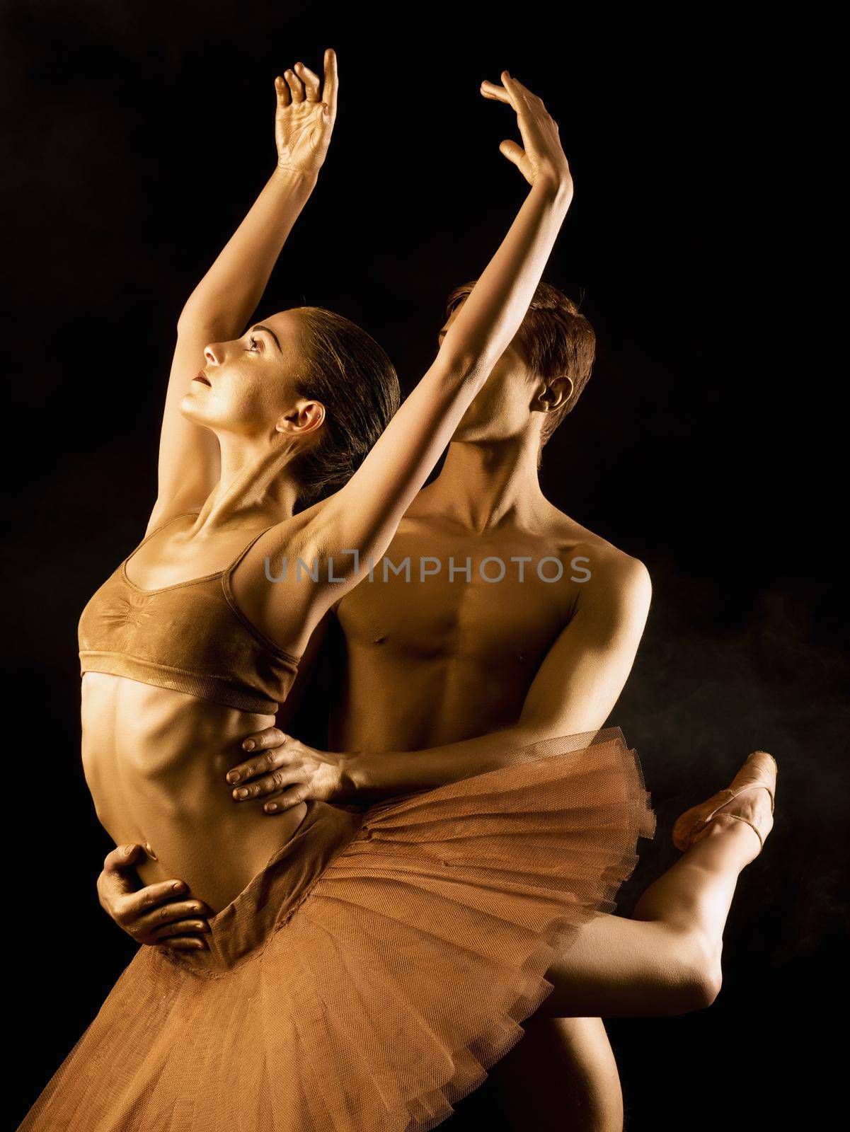 Professional, emotional ballet dancers on dark scene performed by sexual couple with golden body art.Shining gold skin.Pair depicts love and passion on stage.