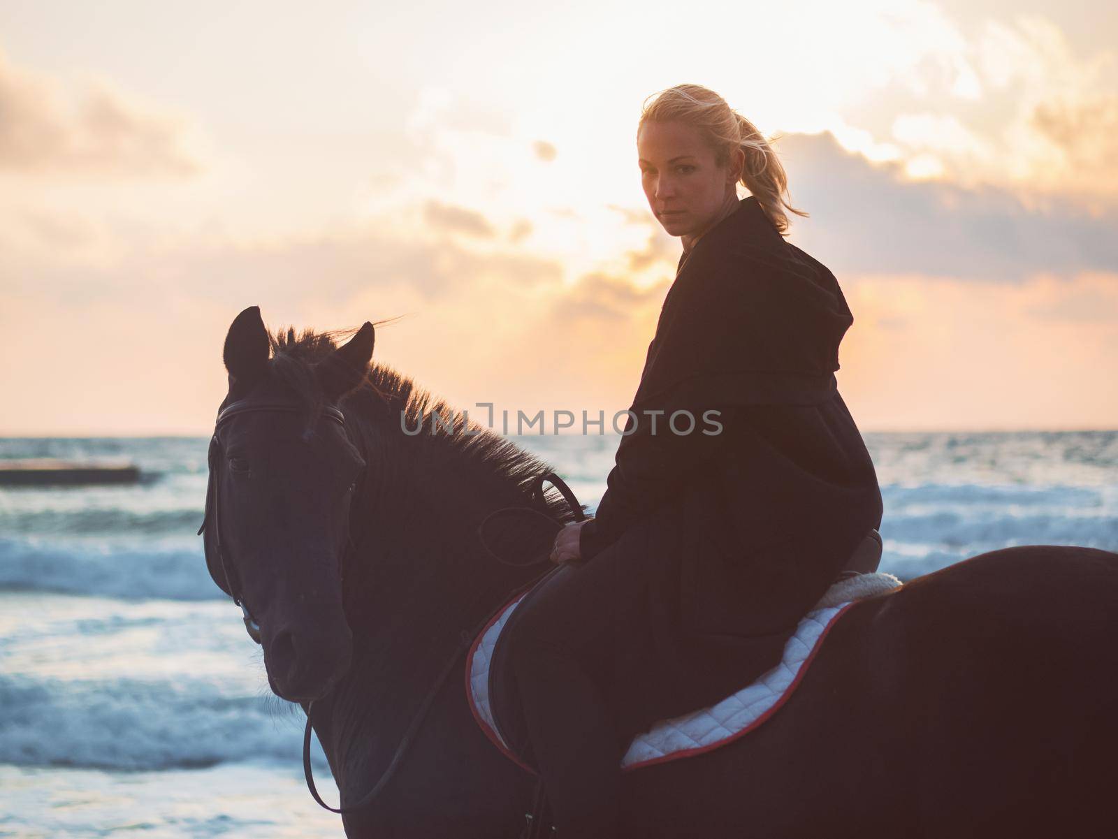 woman sitting on black horse at sea beach by kristina_kokhanova
