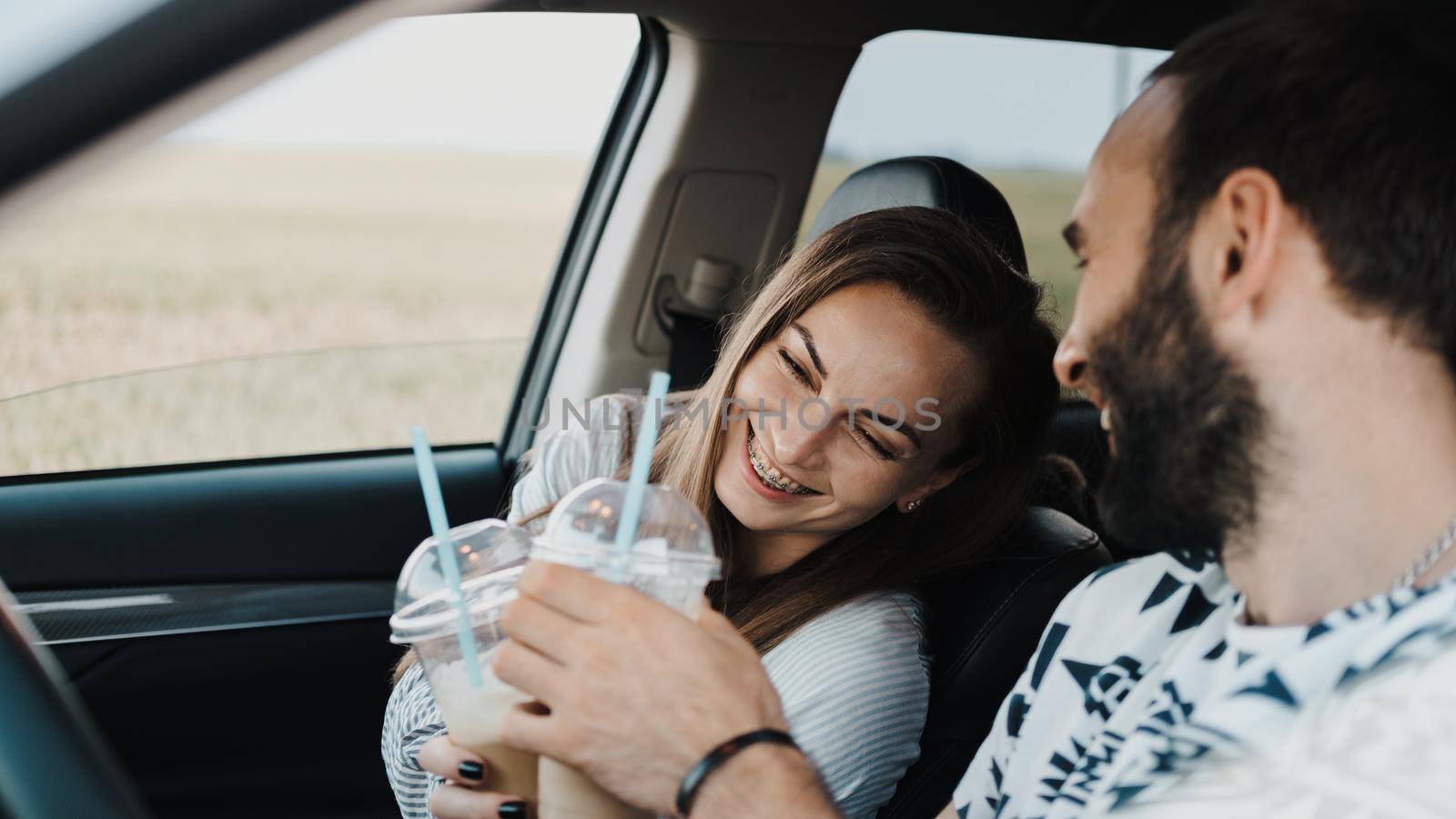 Caucasian cheerful woman sitting inside car and drinking coffee with her boyfriend, happy middle-aged couple on road trip by Romvy