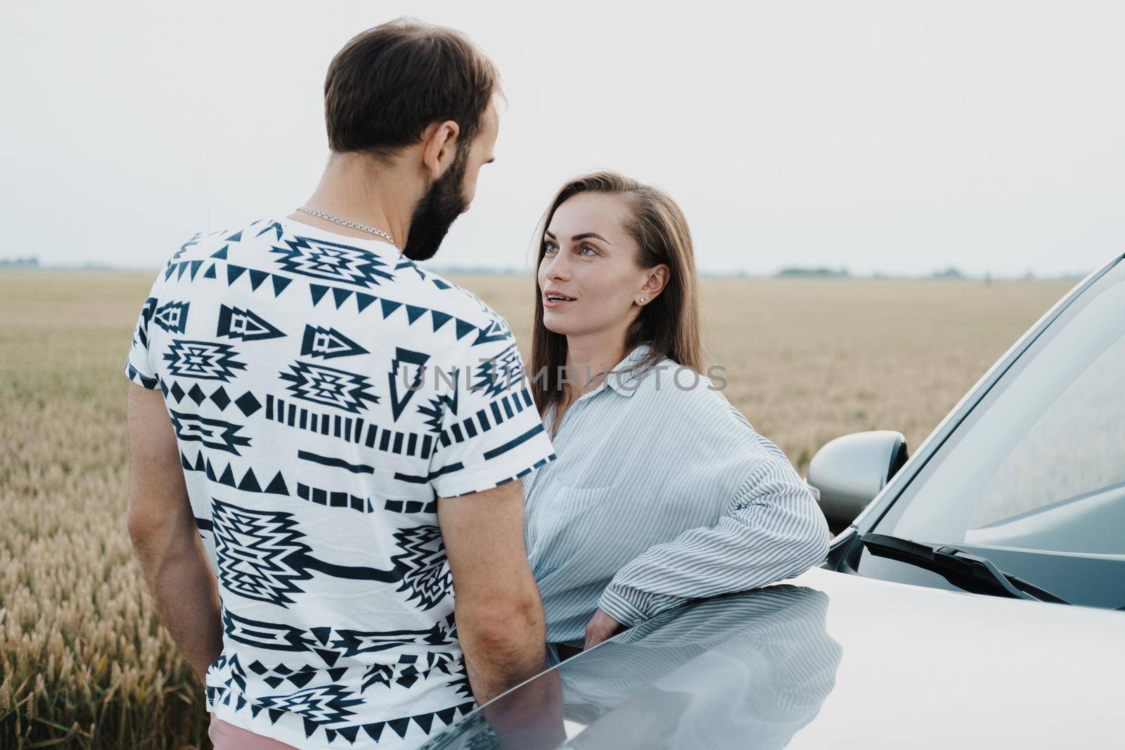 Caucasian woman and man having conversation outdoors near the car in the field, middle-aged couple on road trip