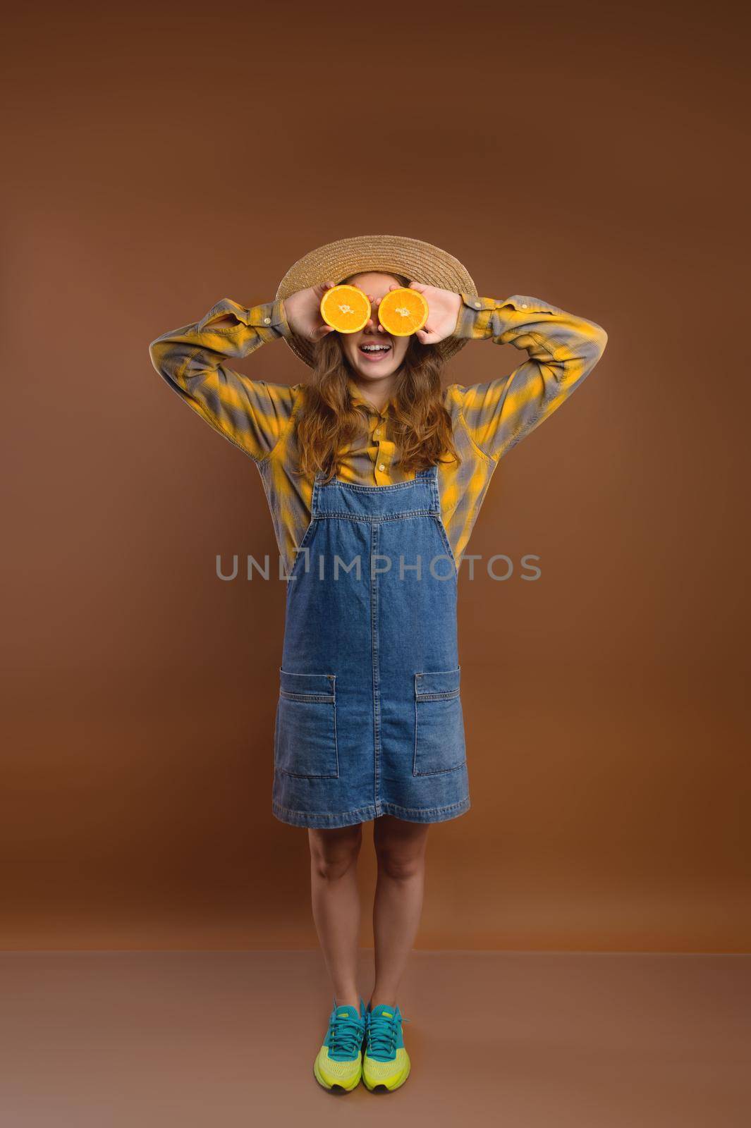 Studio portrait of a cheerful hipster woman going crazy making a funny face and covering her eyes with oranges.