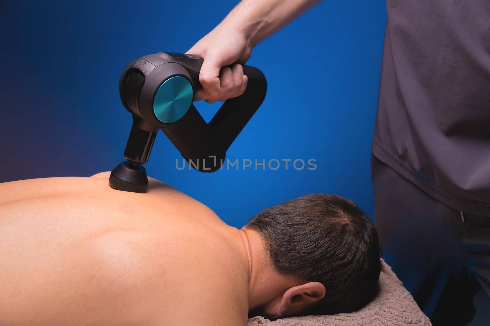 Physiotherapist treats the spine and back of a man with a massage percussion device. Physiotherapy, close-up, massage therapist.