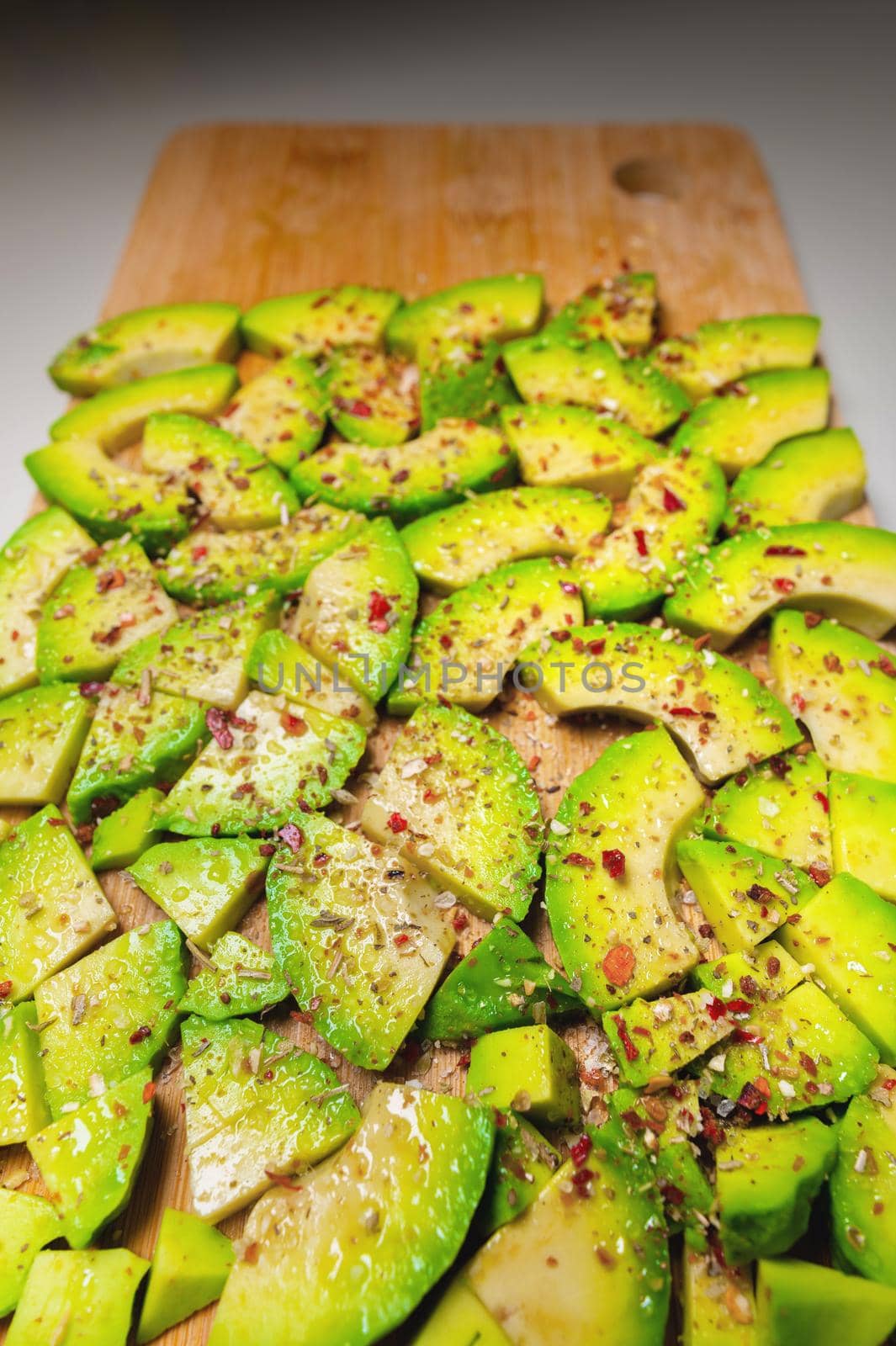 Avocado slices on a wooden textured background sprinkled with spices, bright accent. View from above.
