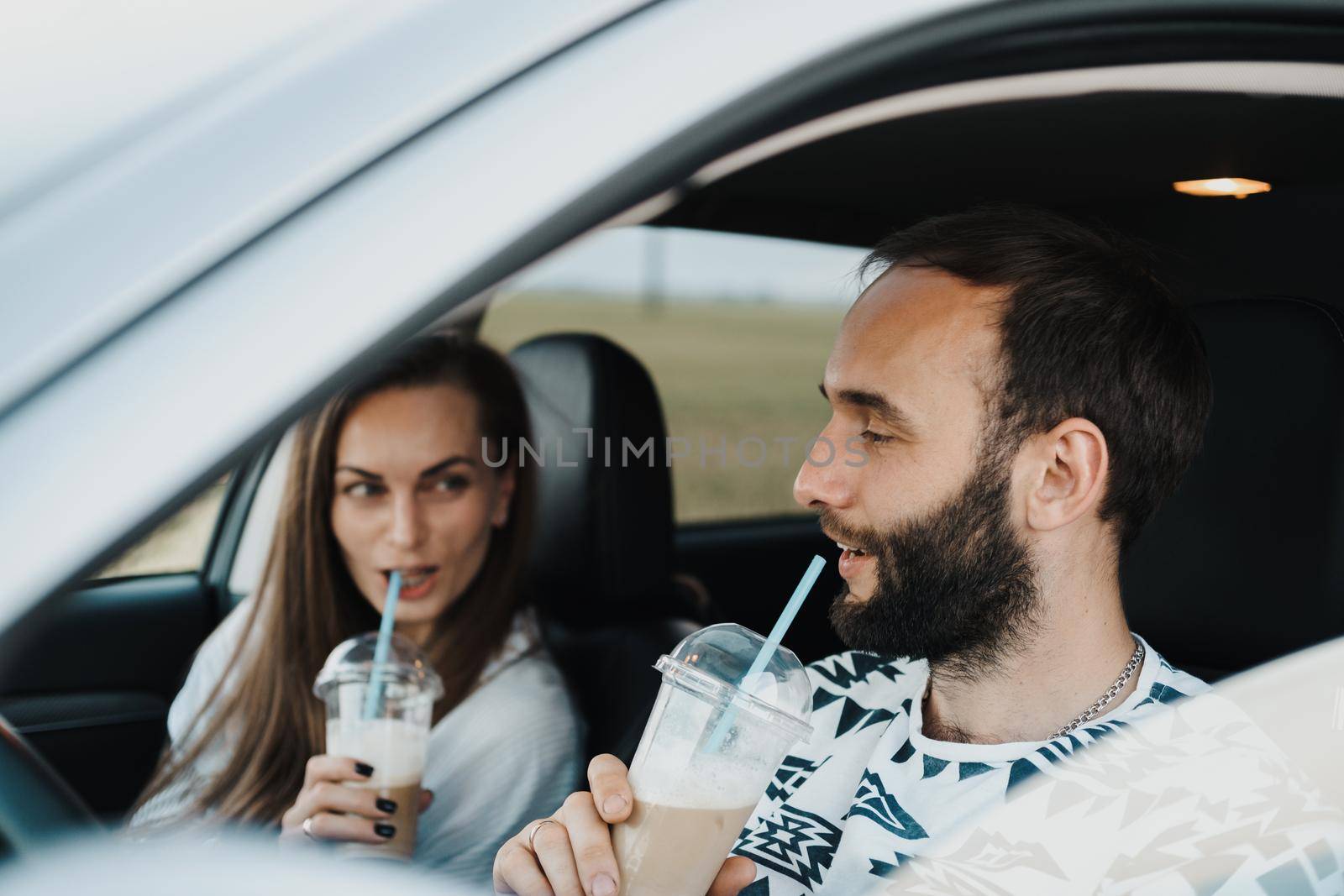 Caucasian handsome man sitting inside car and drinking coffee with his girlfriend, happy middle-aged couple on road trip